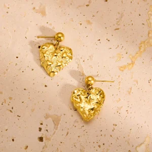 Gold textured heart drop earrings on stone background